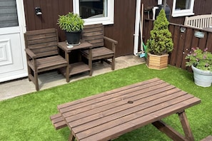 A wooden patio with a table and chairs, a potted plant, and a small garden area with artificial grass. - Cozy Seaside Chalet in Bridlington (Bridlington)