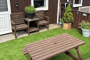 A wooden bench and table set on artificial grass, with a potted plant and a small tree in the background. - Cozy Seaside Chalet in Bridlington (Bridlington)