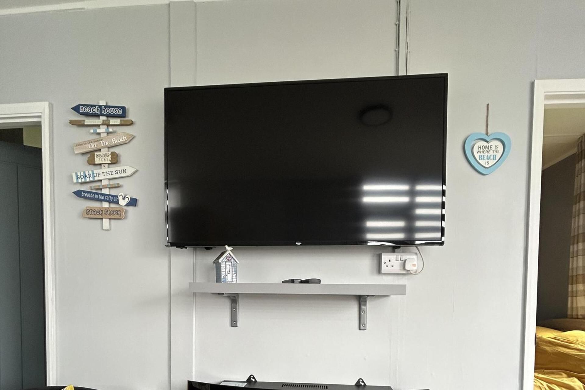 A flat-screen TV mounted on a wall with a shelf below it.