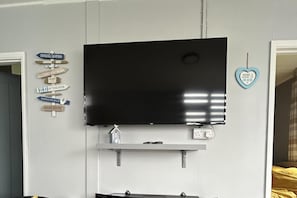 A flat-screen TV mounted on a wall with a shelf below it. - Cozy Seaside Chalet in Bridlington (Bridlington)