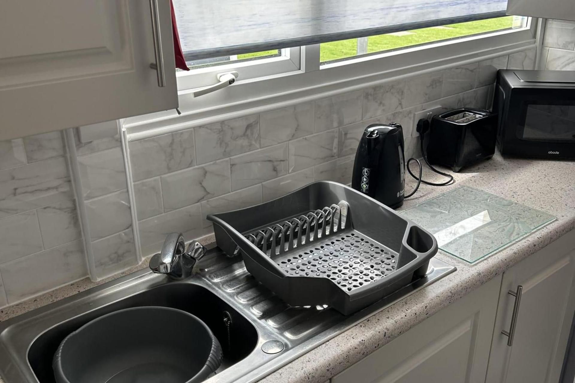 A kitchen with a sink, a black appliance on the counter, and a window with a view of greenery.