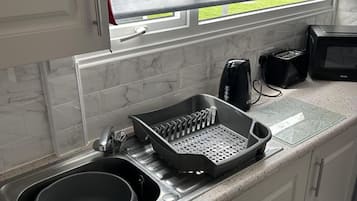 Una cocina con un lavabo, un electrodoméstico negro sobre la encimera y una ventana con vistas a la vegetación.