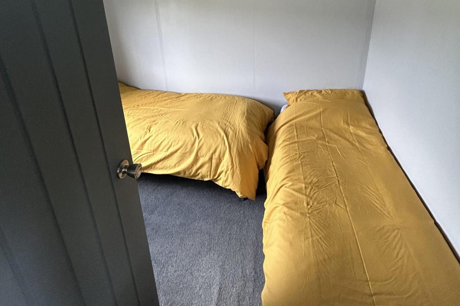 A room with two beds, one with a yellow bedspread and the other with a grey one.