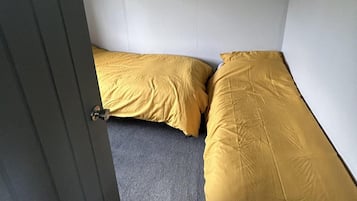 Una habitación con dos camas, una con una colcha amarilla y la otra con una gris.