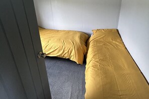 Ein Zimmer mit zwei Betten, eines mit einer gelben Decke und das andere mit einer grauen.