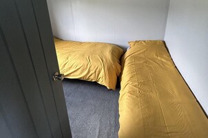 Una habitación con dos camas, una con una colcha amarilla y la otra con una gris.