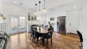 Una cocina moderna con armarios blancos, un refrigerador de acero inoxidable y un comedor con una mesa y sillas de madera.