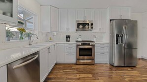 Una cocina moderna con armarios blancos, electrodomésticos de acero inoxidable, lavavajillas y piso de madera.