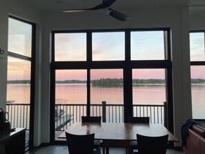A dining area with a large window overlooking a body of water and trees.