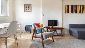 Een moderne woonkamer met een eethoek, een grijze bank, een houten salontafel, een kleurrijke fauteuil en een lijstwerk kunstwerk aan de muur.