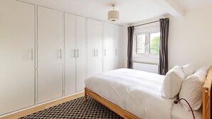Een slaapkamer met een bed, een kledingkast, een raam met gordijnen en een kamerbreed tapijt.