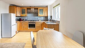 Een moderne keuken met houten kastjes, een roestvrijstalen fornuis en een eethoek met een houten tafel en stoelen.