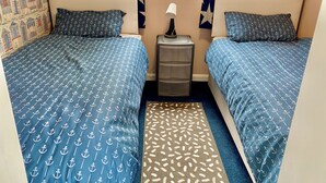 A room with two beds, each with blue bedding featuring anchor patterns. There is a small bedside table with a lamp, a star decoration on the wall, and a patterned rug on the floor. - Large 3 bed Chalet -sleeps 6- dog Friendly- Garden (Bridlington)