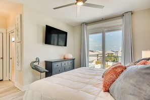 Un dormitorio con una cama grande, un ventilador de techo, un televisor de pantalla plana y vistas al exterior.