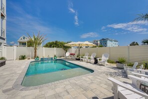 Una piscina con borde empinado y baldosas, rodeada de sillas y sombrillas blancas, con vistas a casas al fondo.