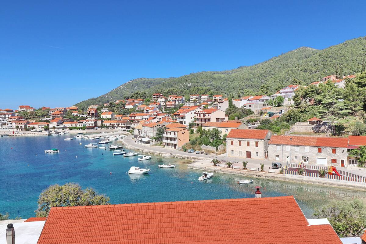 A coastal town with buildings along the waterfront, boats docked in the harbor, and a hillside in the background.