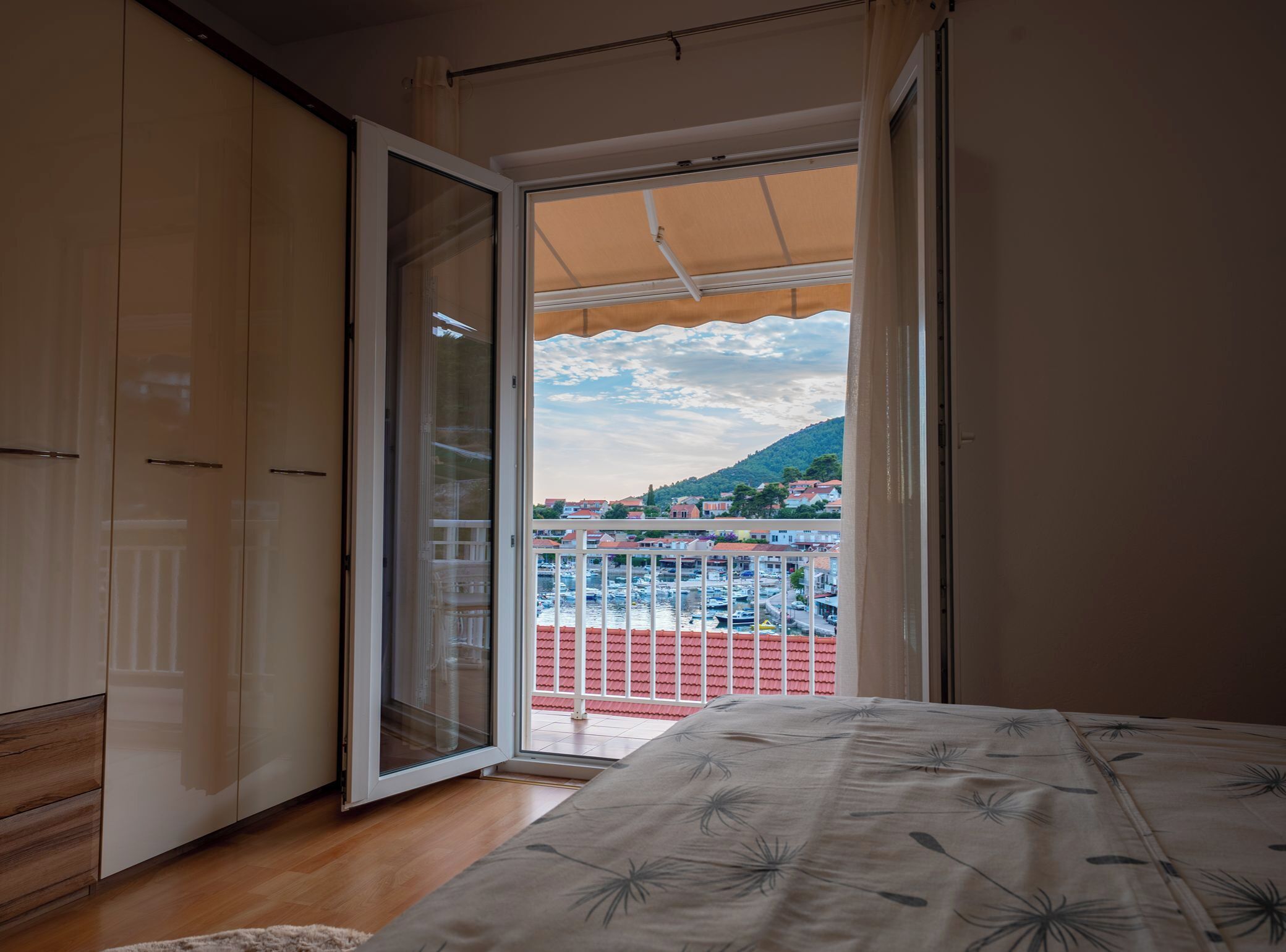 A bedroom with a balcony, wooden wardrobe, and a bed with a floral bedspread.