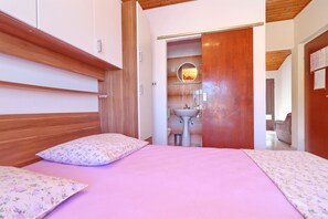 A bedroom with a wooden headboard, a bed with pink bedding, and a bathroom visible through an open door.