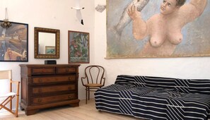 Een kamer met een houten dressoir, een stoel, een gestreepte bank en een groot schilderij aan de muur.