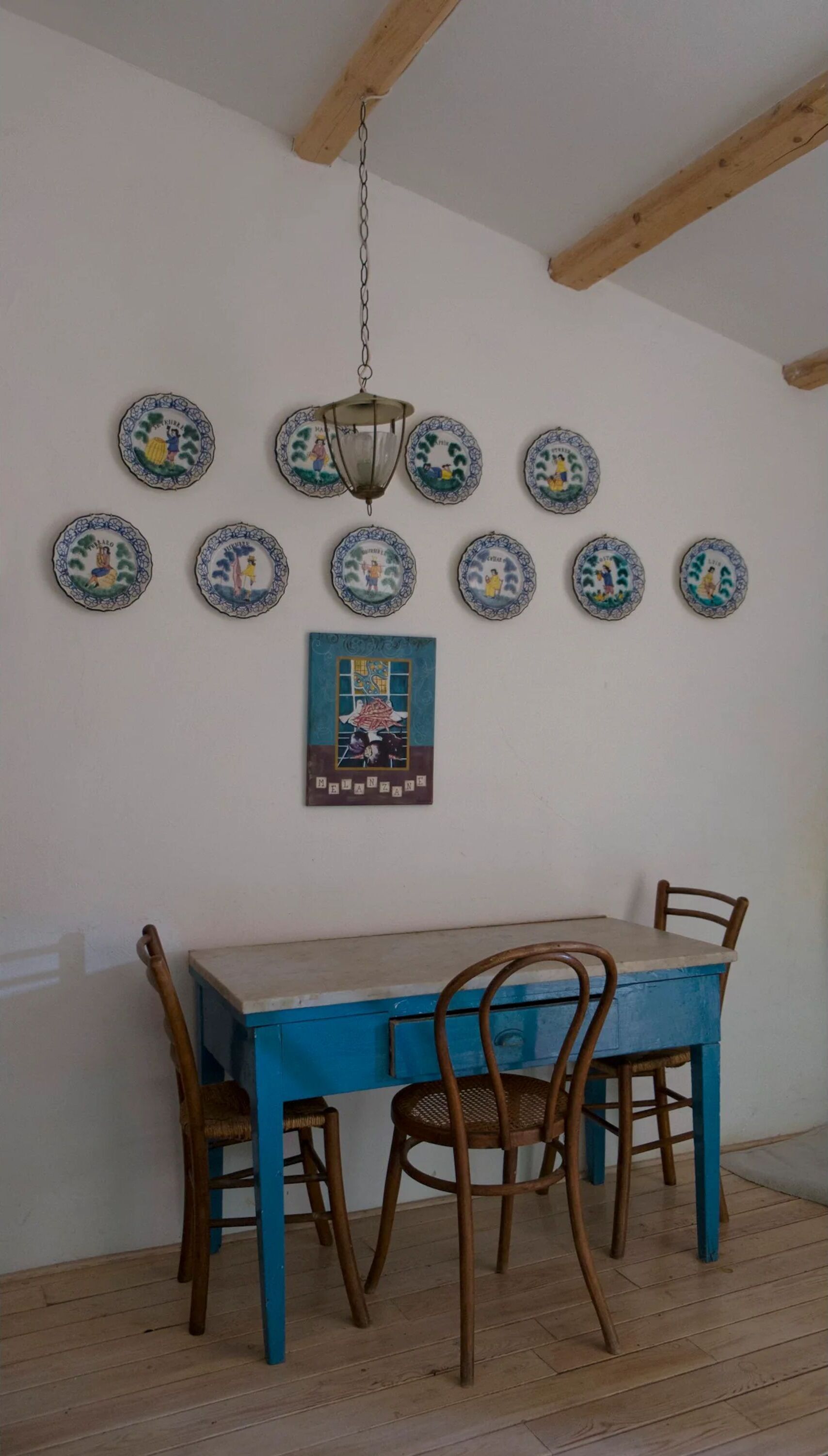 A dining area with a blue table and wooden chairs, a hanging lantern, and a wall decorated with circular plates.