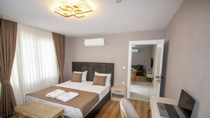A hotel room with a bed, bedside table, chair, desk with a laptop, and an air conditioning unit. - Luxury Life Suites (Istanbul)