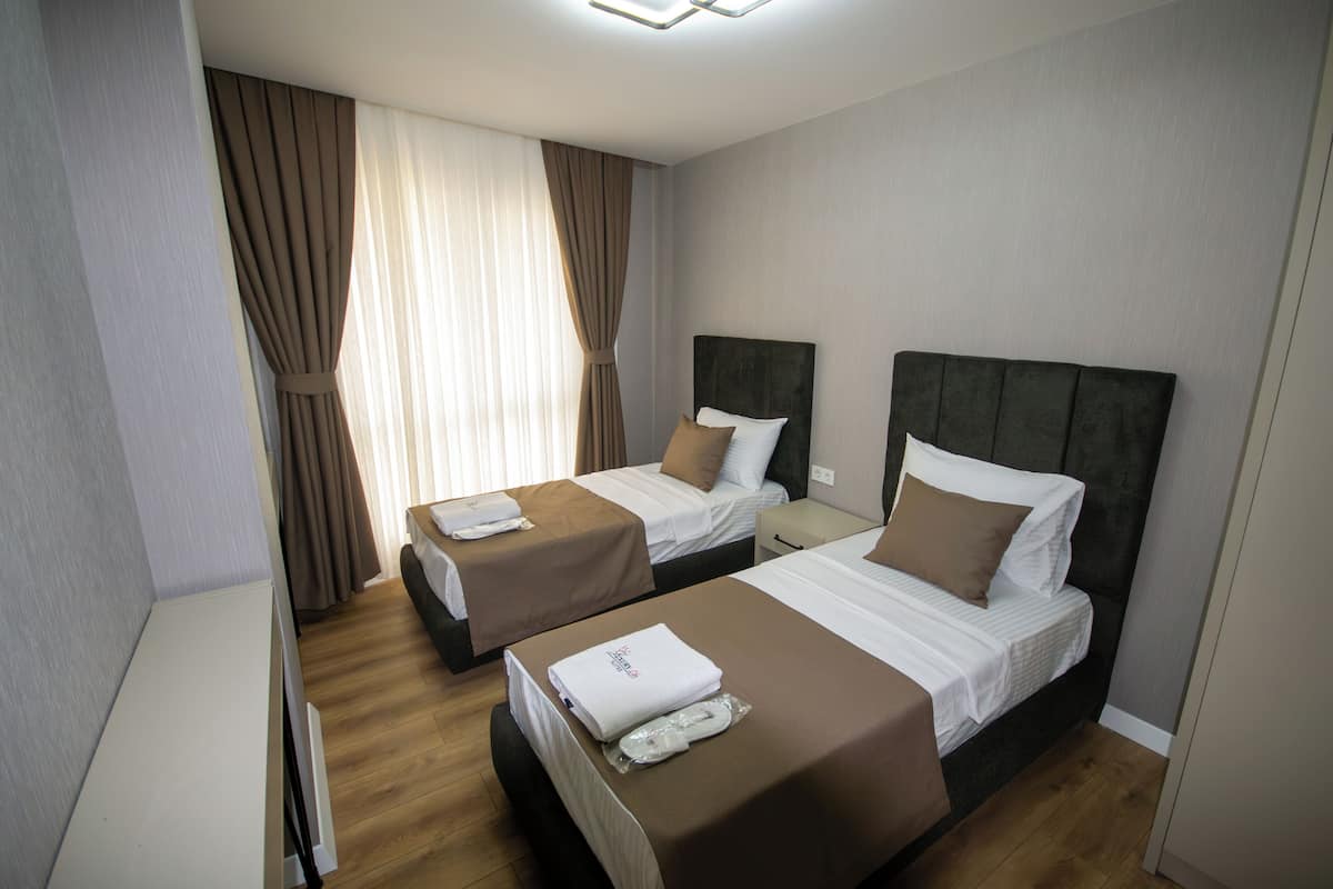 A hotel room with two beds, a wooden floor, and a large window with curtains.