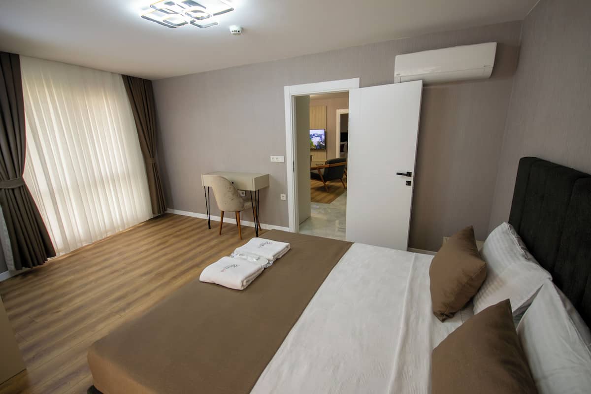 A hotel room with a bed, a desk, and a chair. There is a television in the corner and an air conditioning unit on the wall.