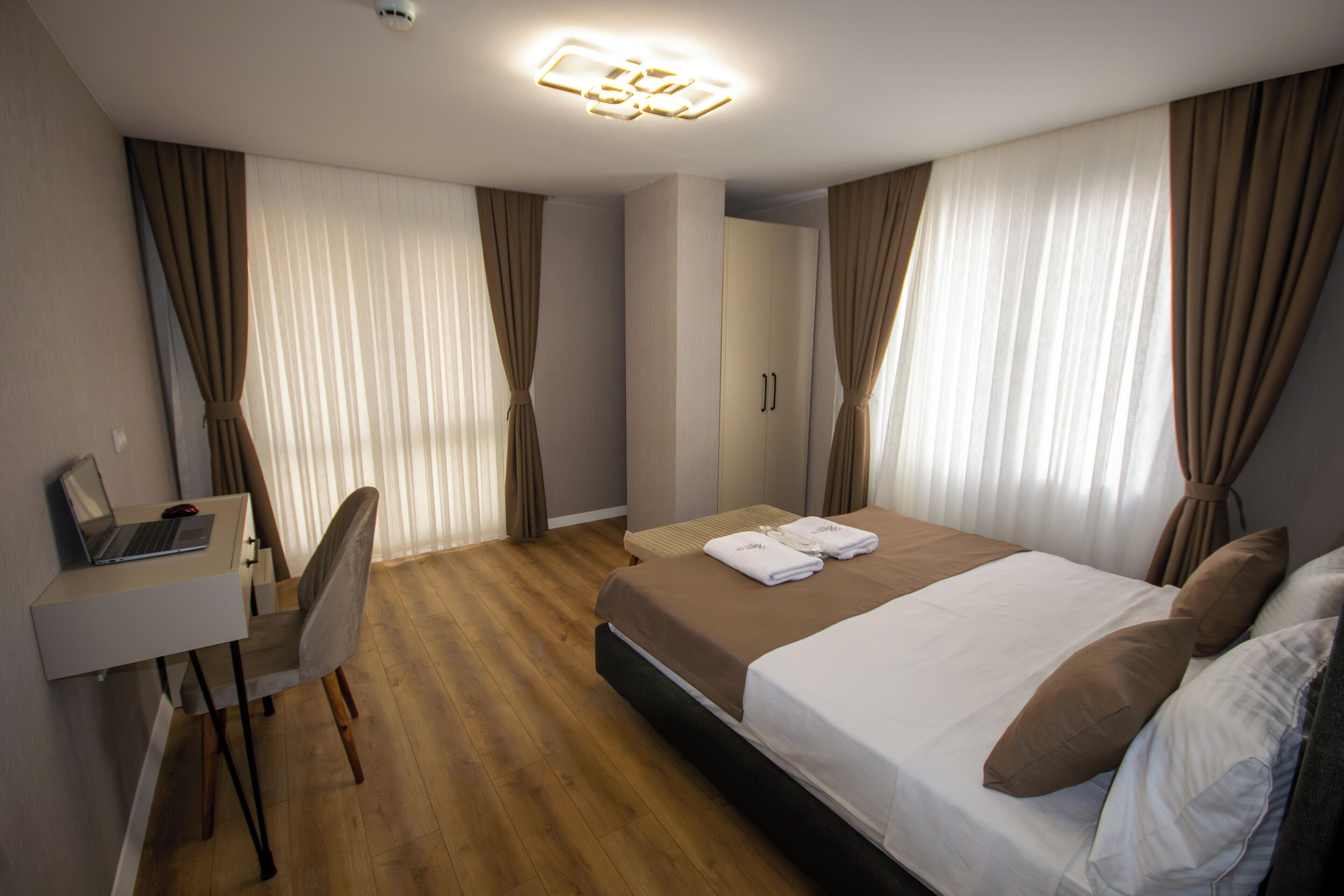 A hotel room with a bed, a desk with a laptop, a chair, and a wardrobe.