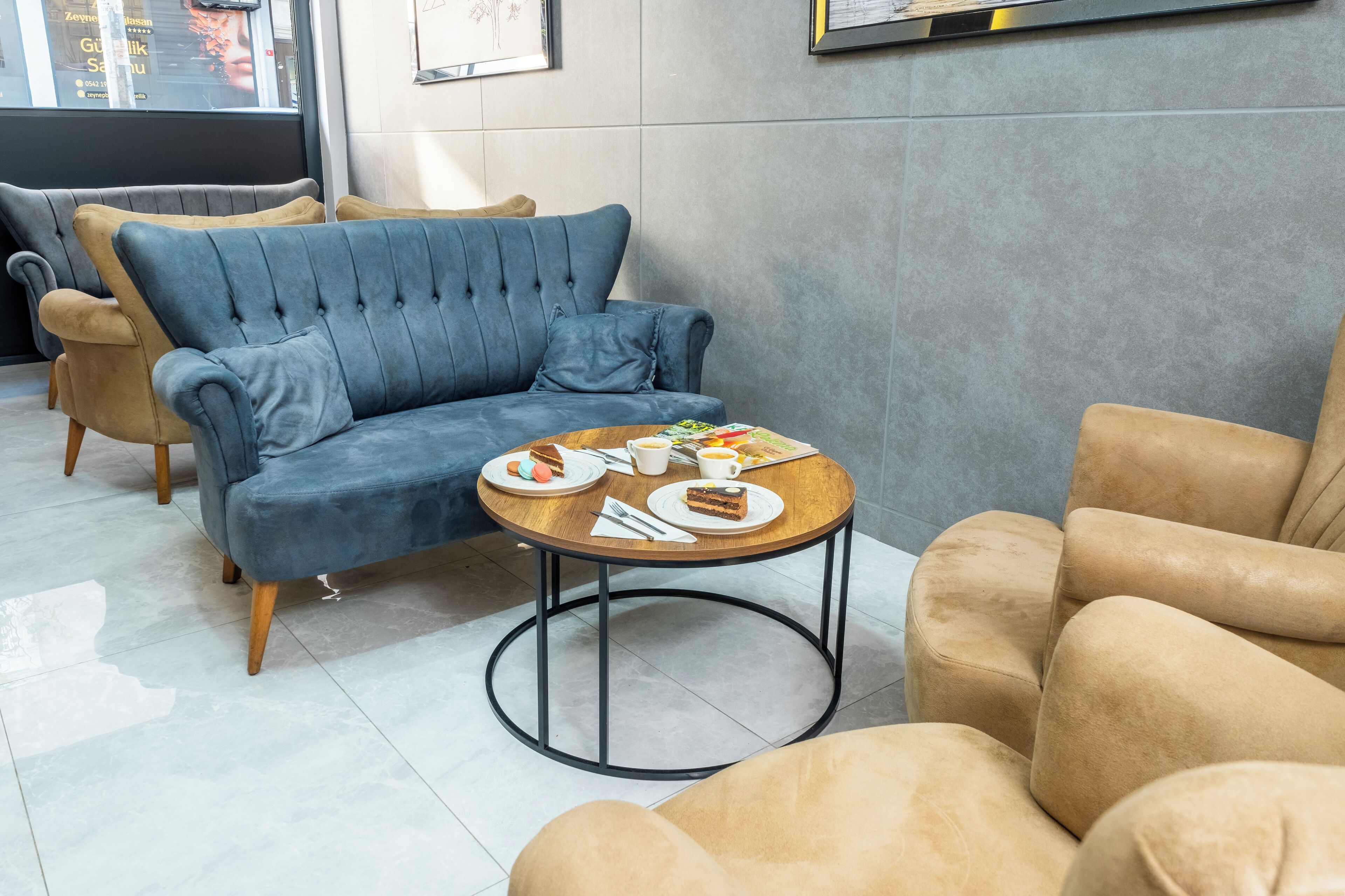 Un área de descanso moderna con un sofá azul, una mesa de centro de madera con comida y bebidas, y sillones beige.