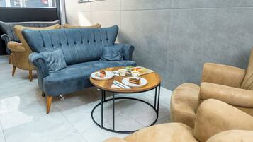 Un área de descanso moderna con un sofá azul, una mesa de centro de madera con comida y bebidas, y sillones beige.