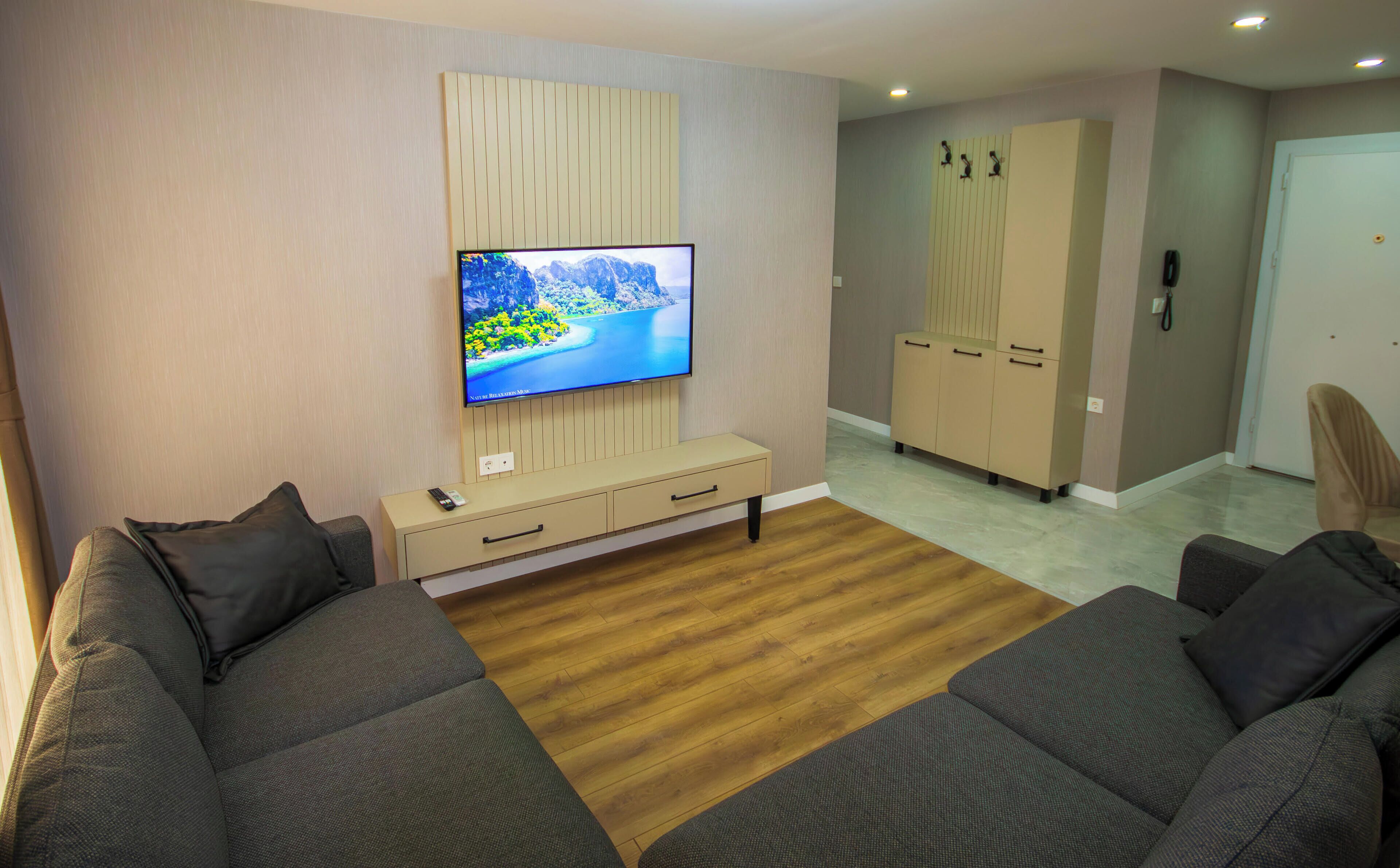 Una sala de estar moderna con televisor de pantalla plana, mueble de entretenimiento color beige, piso de madera y sofá gris.