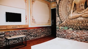 A room with a brick wall, a flat-screen TV mounted on the wall, a small wooden table, and a large mural of a meditating figure. - Pablo Suit Hotel (Istanbul)