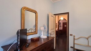 A hotel room with a wooden dresser, a large mirror, a television, and a door leading to another room.