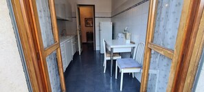 A narrow kitchen with white cabinets, a white countertop, and a dining area with a white table and chairs. - Casa Matilda Old Style (Rome)