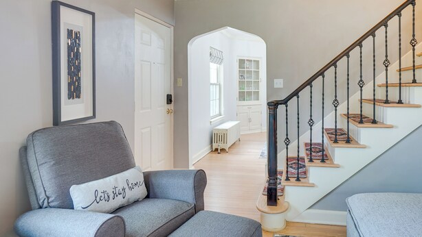 A living room with a gray armchair, a framed picture on the wall, and a staircase with patterned risers. - Walkable Thiensville Retreat Near Hiking! (Mequon)