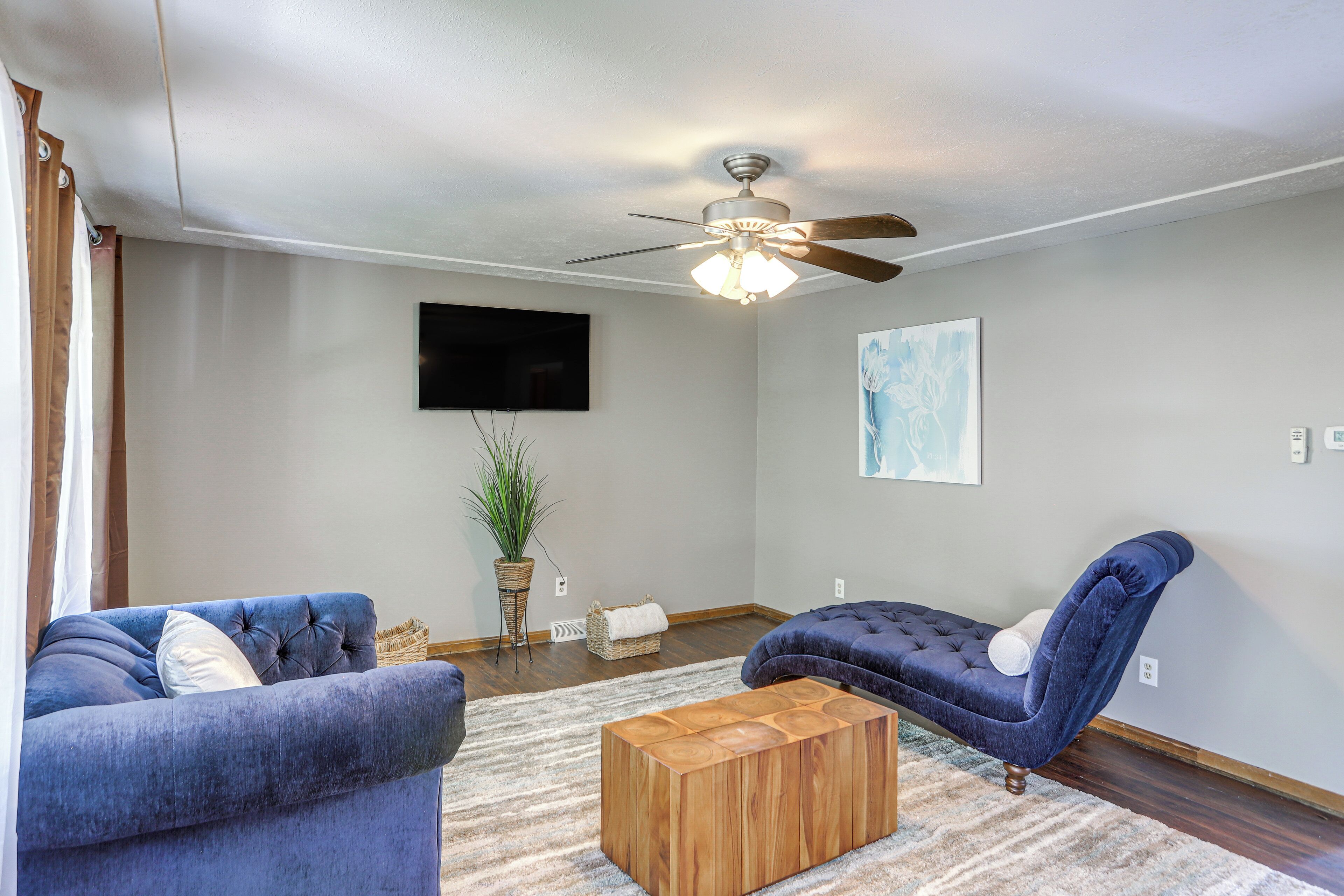 A living room with two blue sofas, a wooden coffee table, a ceiling fan, a flat-screen TV, and a potted plant.