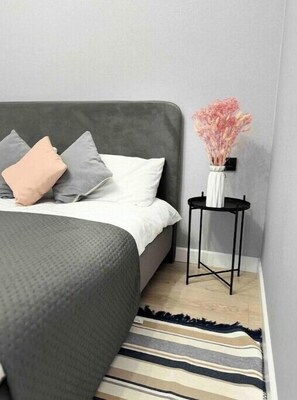 Relax in a serene bedroom with a large bed, a black side table, and a striped rug.