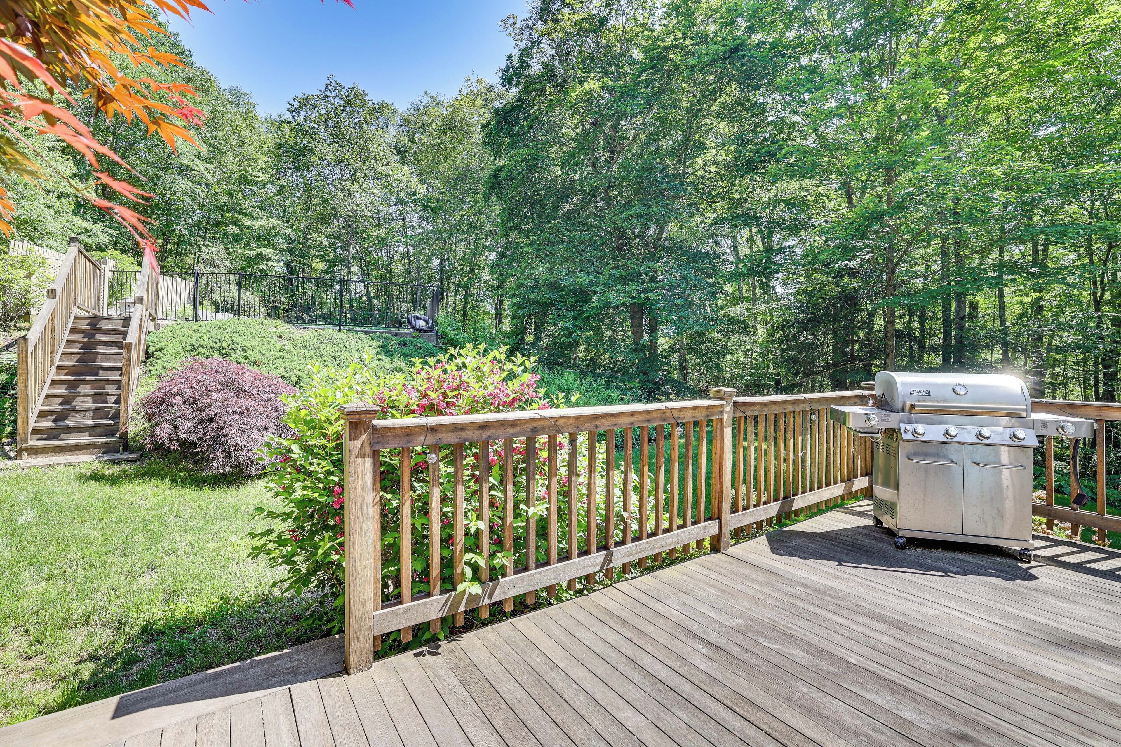 A wooden deck with a barbecue grill, surrounded by lush greenery and a wooden fence.