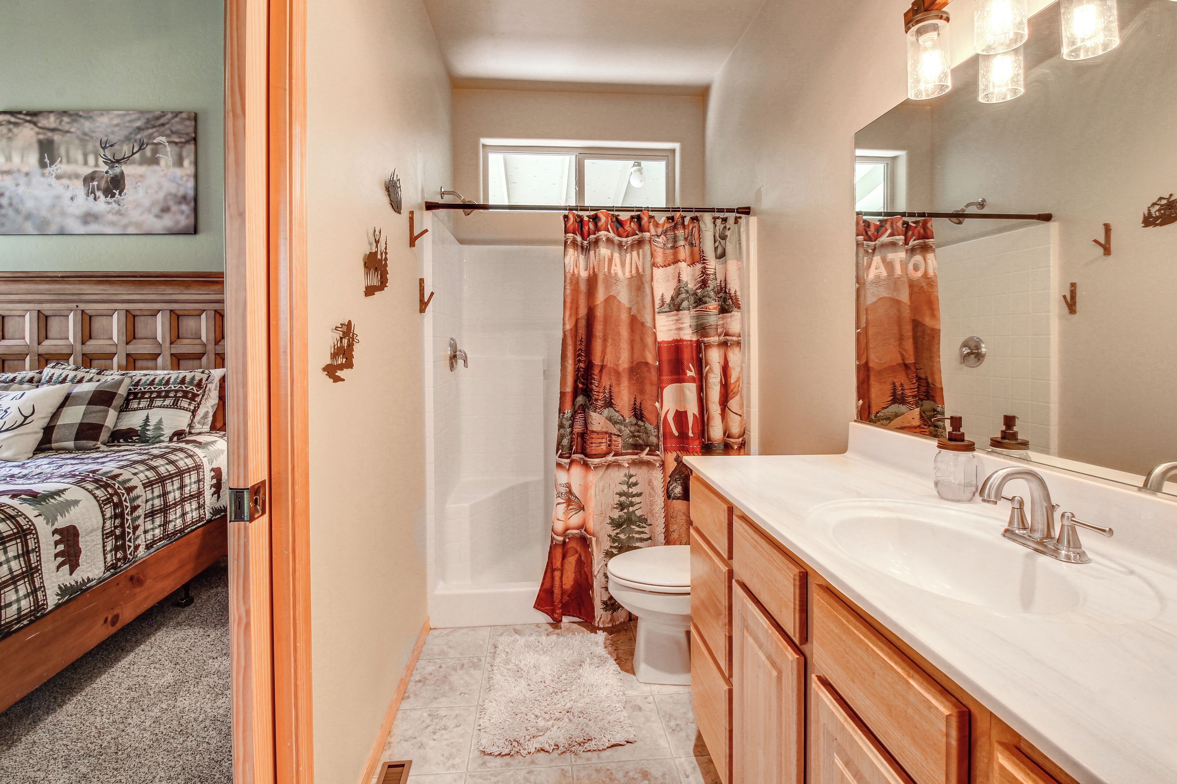 A bathroom with a shower curtain, toilet, sink, and a bed with a headboard.