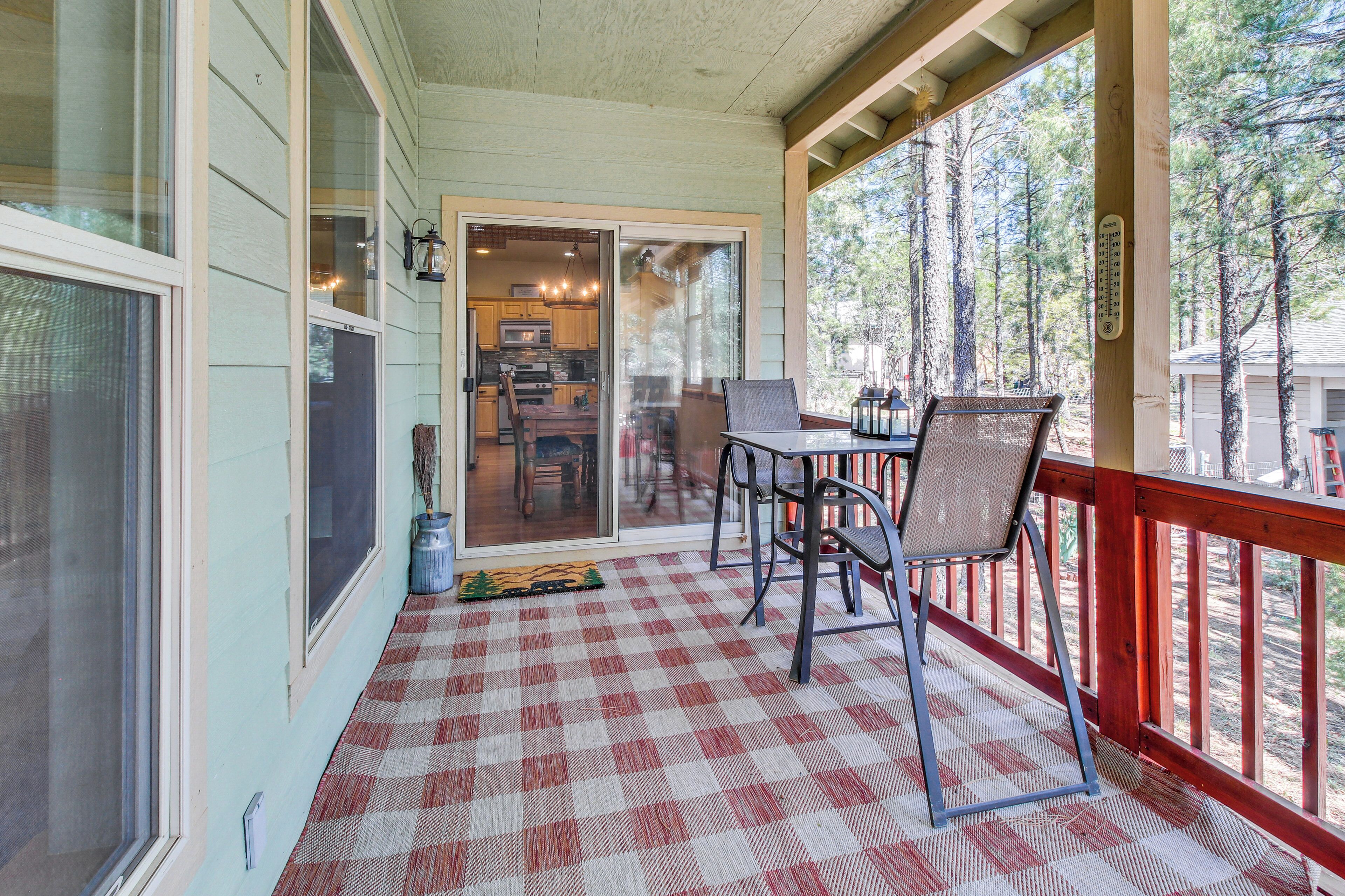 A covered porch with a checkered floor, a dining table with chairs, and a view of the kitchen through glass doors.