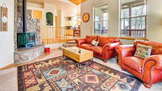 A cozy living room with a stone fireplace, leather sofas, and a patterned rug. - Walk to Rainbow Lake: Peaceful Cabin w/ Fire Pit (Lakeside)