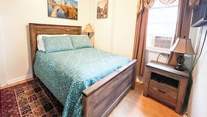 A bedroom with a bed, a wooden nightstand, a television, and a window with curtains. - Sweet Small Studio (Philadelphia)