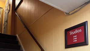 A staircase with a wooden handrail and a sign indicating 'Studios #103, #104, #105'. - Sweet Small Studio (Philadelphia)