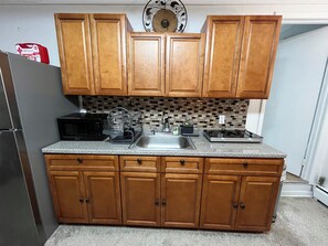 A kitchen with wooden cabinets, a granite countertop, a black microwave, a dish rack, and a stainless steel sink. - Quite Cozy Studio apartment (Philadelphia)
