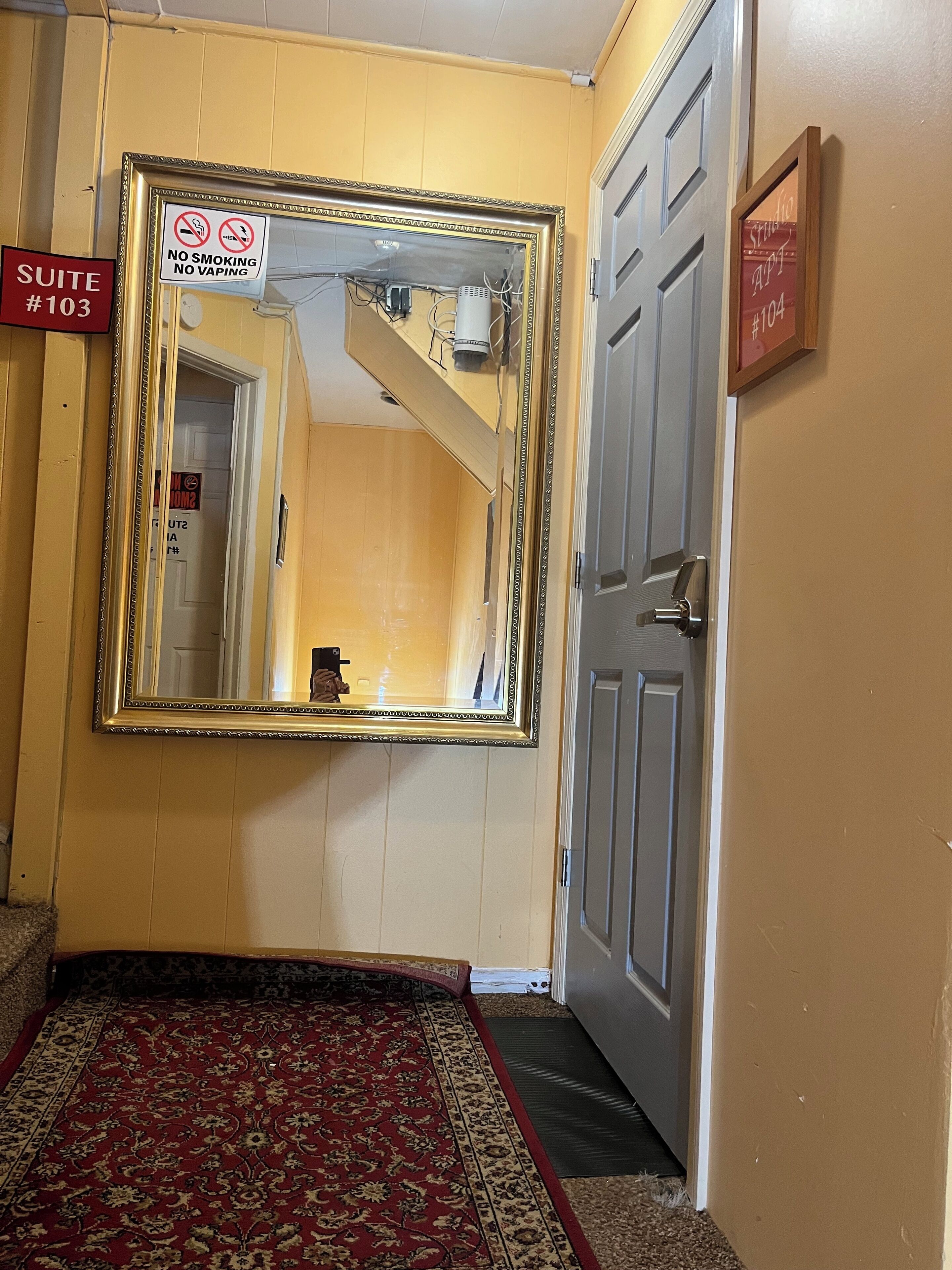 A hallway with a large mirror, a 'No Smoking' sign, a 'Suite #103' sign, and a 'Studio #104' sign.