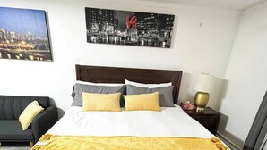 A hotel room with a large bed, a nightstand with a lamp, a couch, and two framed pictures on the wall. - Quite Cozy Studio apartment (Philadelphia)