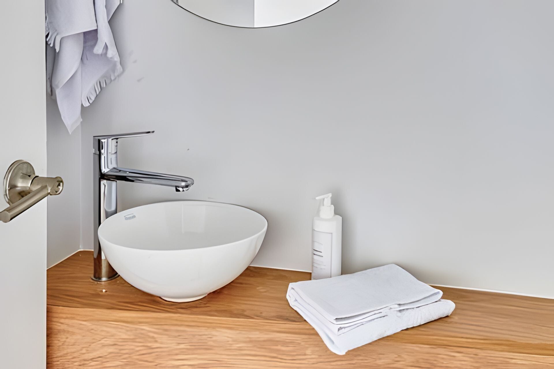 Une salle de bain avec un lavabo blanc, un robinet chromé et un plan de toilette en bois.