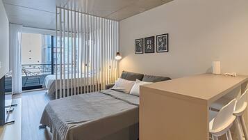 A modern bedroom with a bed, a desk, and a chair. There are three framed pictures on the wall.