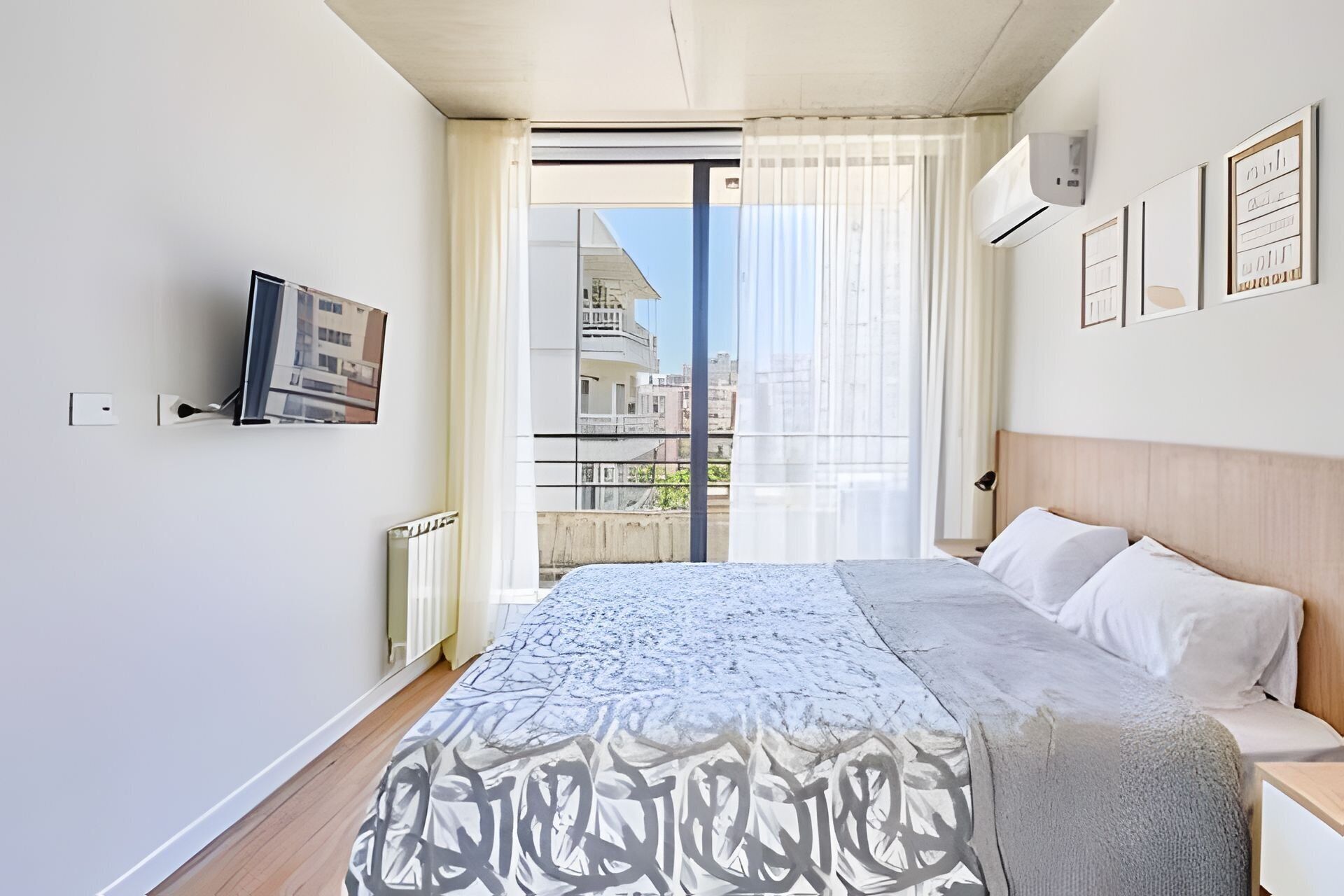 Une chambre d’hôtel moderne, dotée d’un grand lit, d’un téléviseur fixé au mur et offrant une vue sur la ville par la fenêtre.
