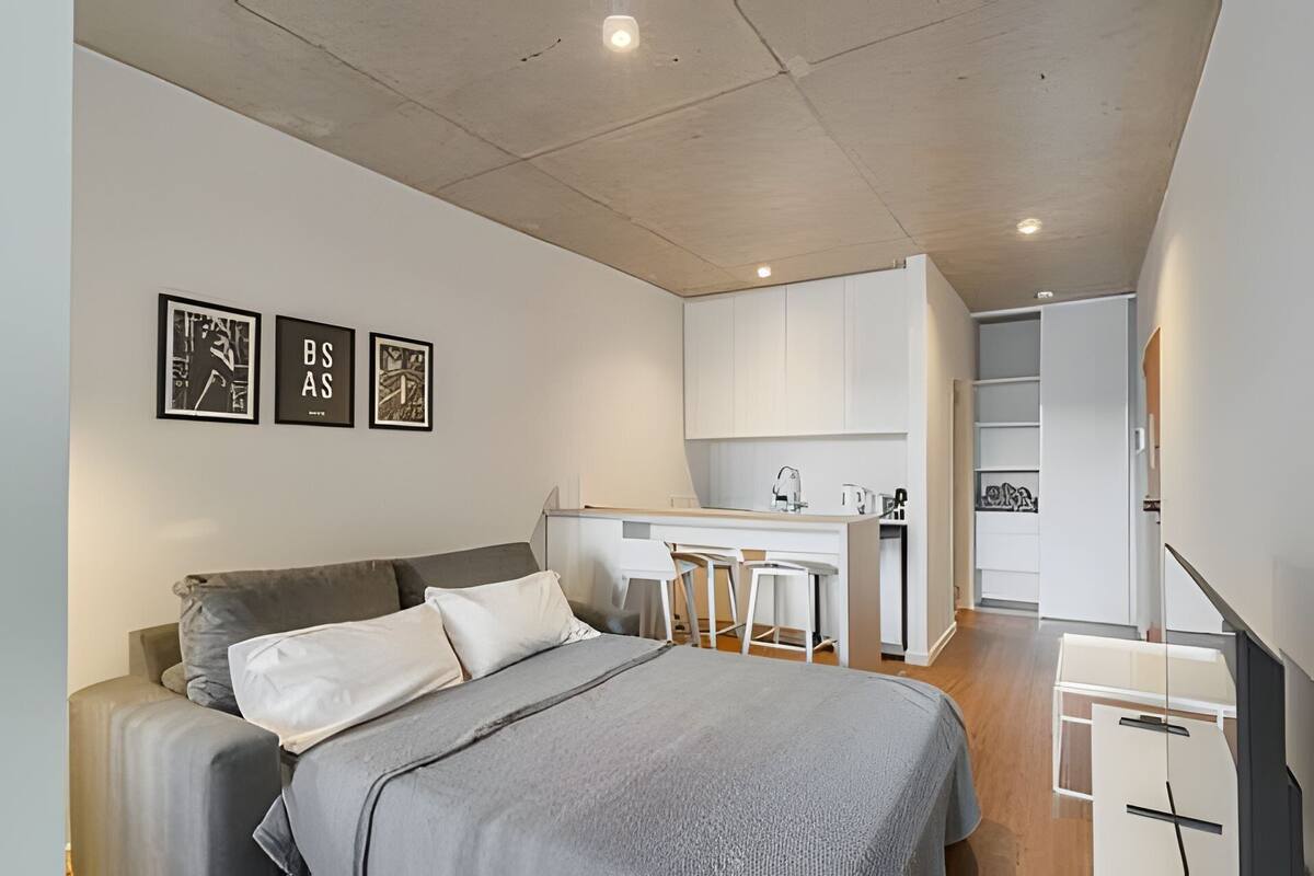 Een moderne slaapkamer met een bed, een kitchenette en een witte garderobe.